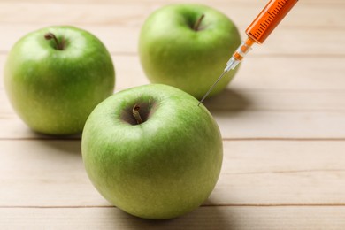 Photo of GMO concept. Injecting green apples with syringe at wooden table, closeup