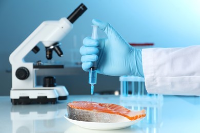 Photo of GMO concept. Scientist injecting something into piece of salmon at table in laboratory, closeup