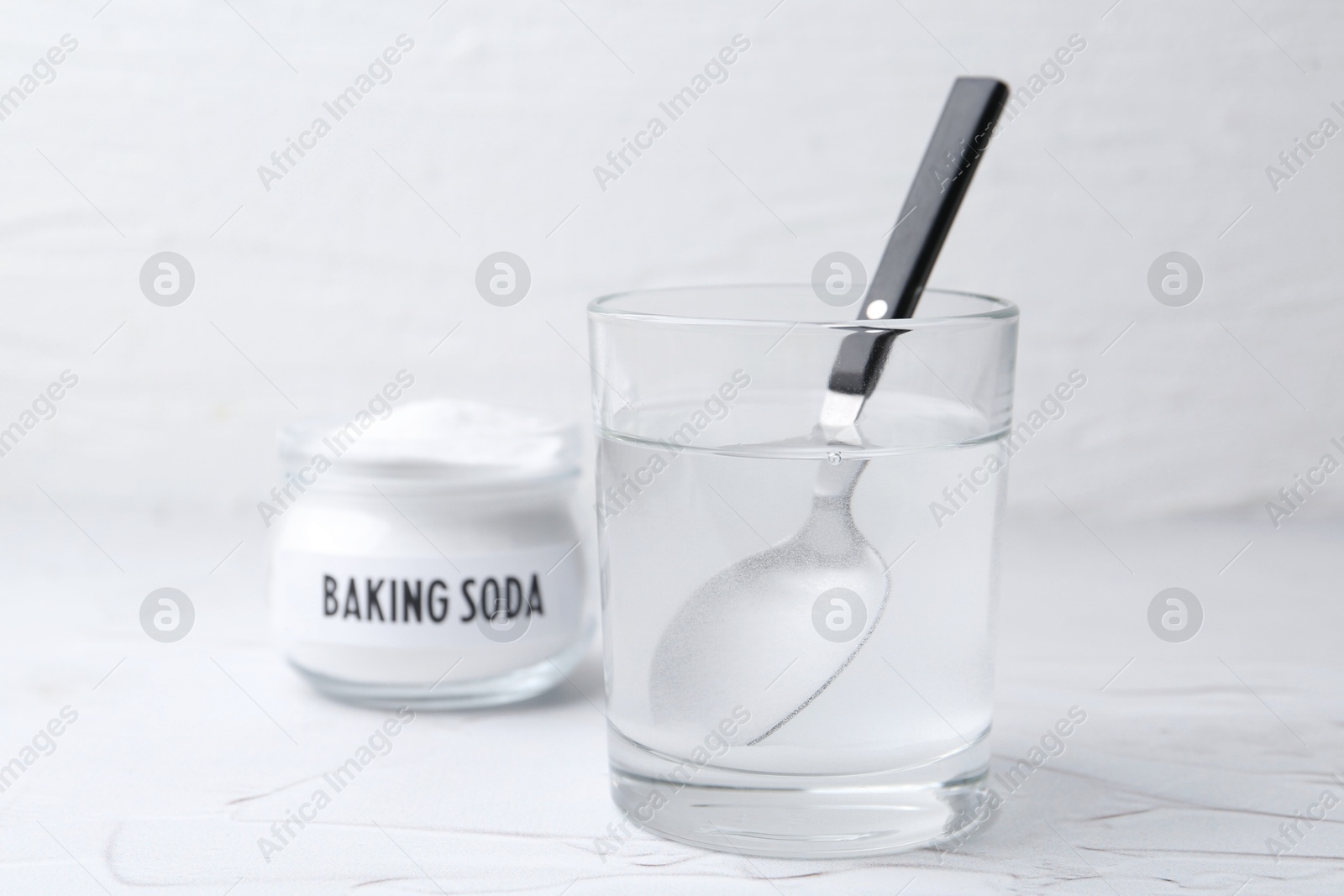 Photo of Glass of water and baking soda on white textured table, selective focus