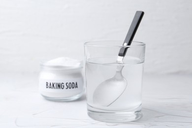 Photo of Glass of water and baking soda on white textured table, selective focus