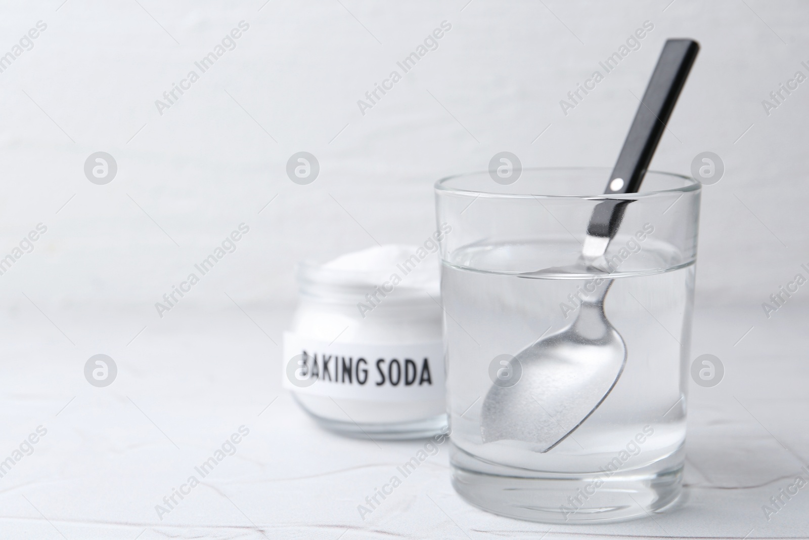 Photo of Glass of water and baking soda on white textured table, selective focus. Space for text