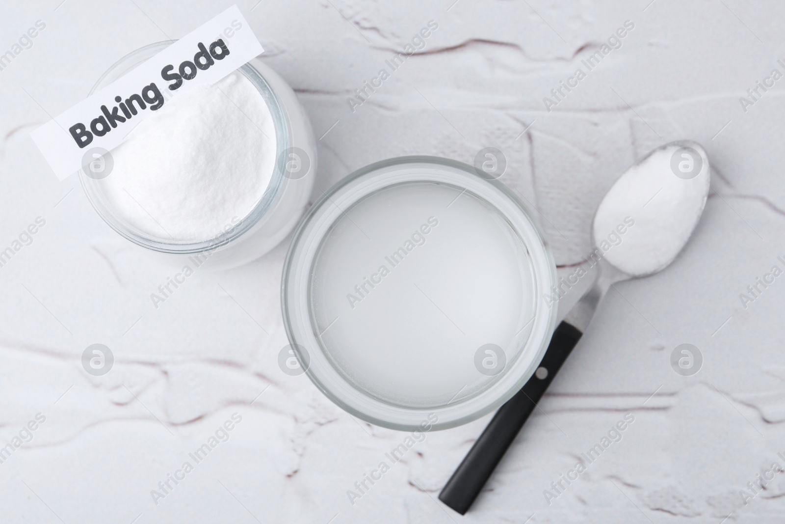 Photo of Glass with water and baking soda on white textured table, top view