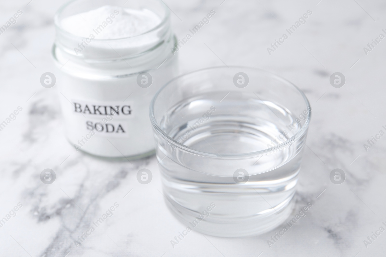 Photo of Glass of water and baking soda on white marble table, selective focus