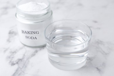 Photo of Glass of water and baking soda on white marble table, selective focus