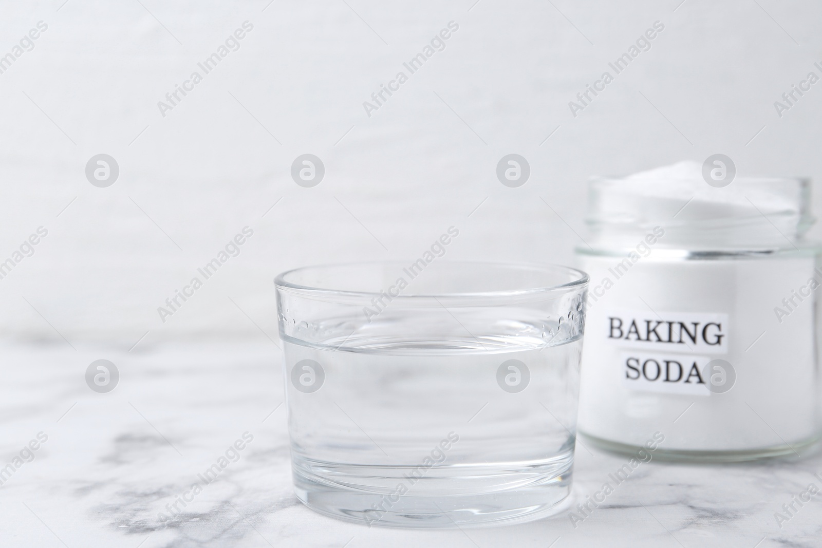 Photo of Glass of water and baking soda on white marble table. Space for text