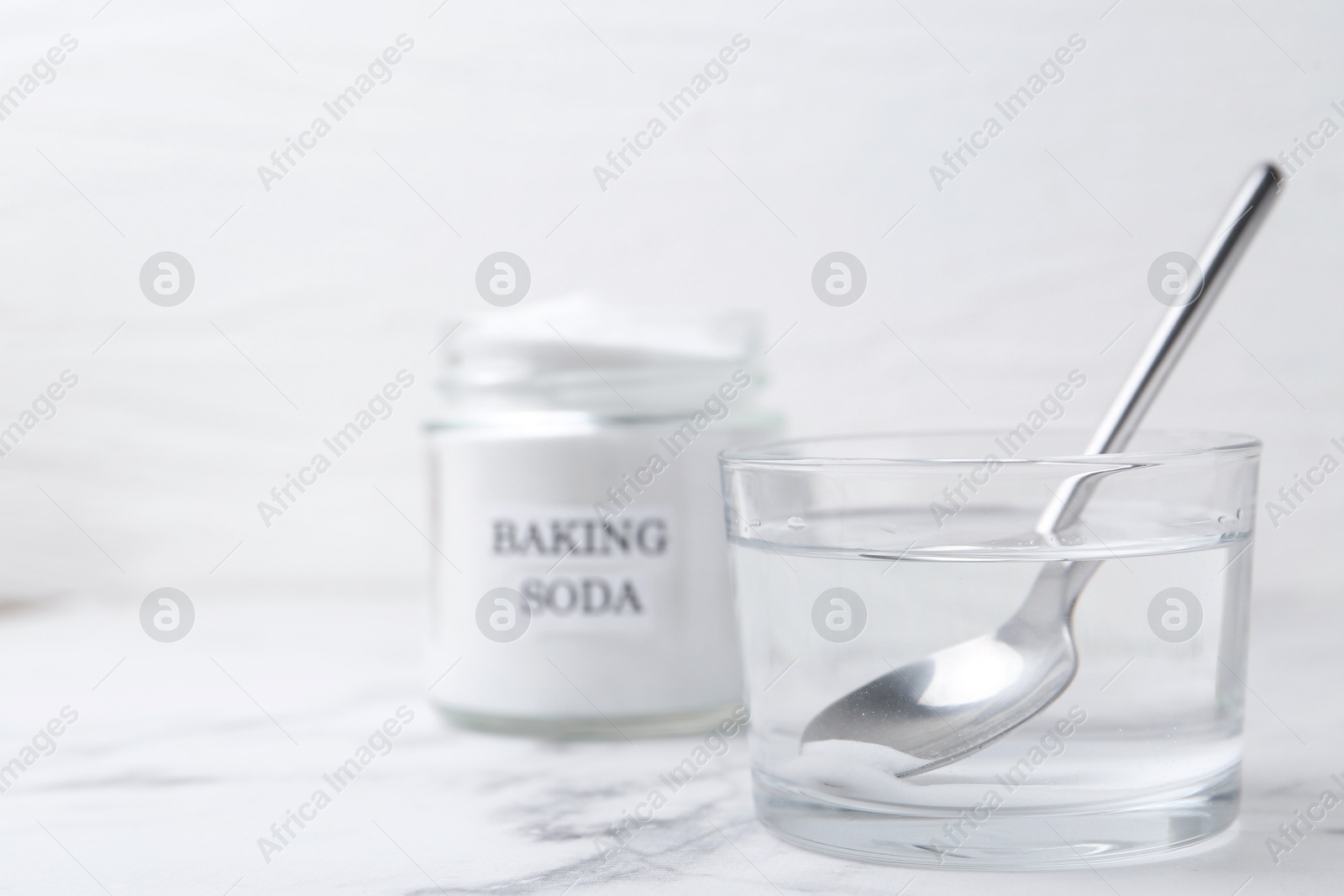 Photo of Glass of water and baking soda on white marble table, selective focus. Space for text