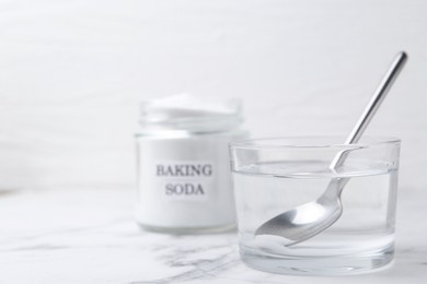 Photo of Glass of water and baking soda on white marble table, selective focus. Space for text