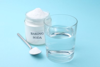 Photo of Glass of water and baking soda on light blue background, selective focus