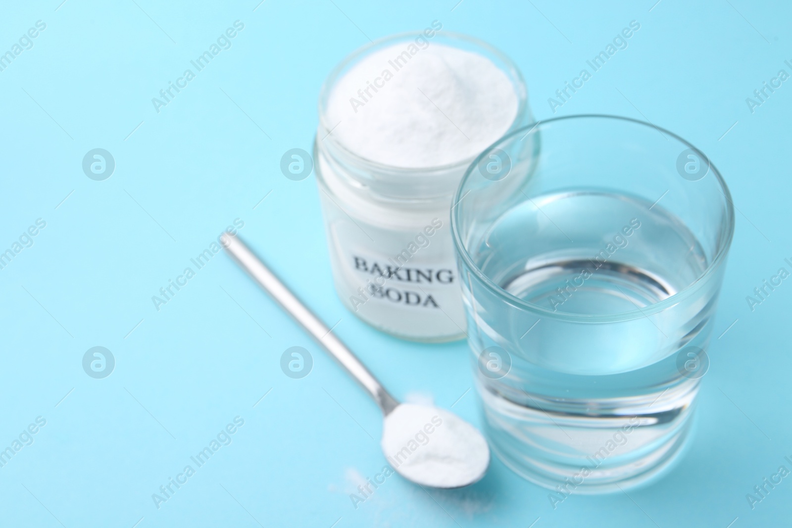 Photo of Glass of water and baking soda on light blue background, selective focus. Space for text