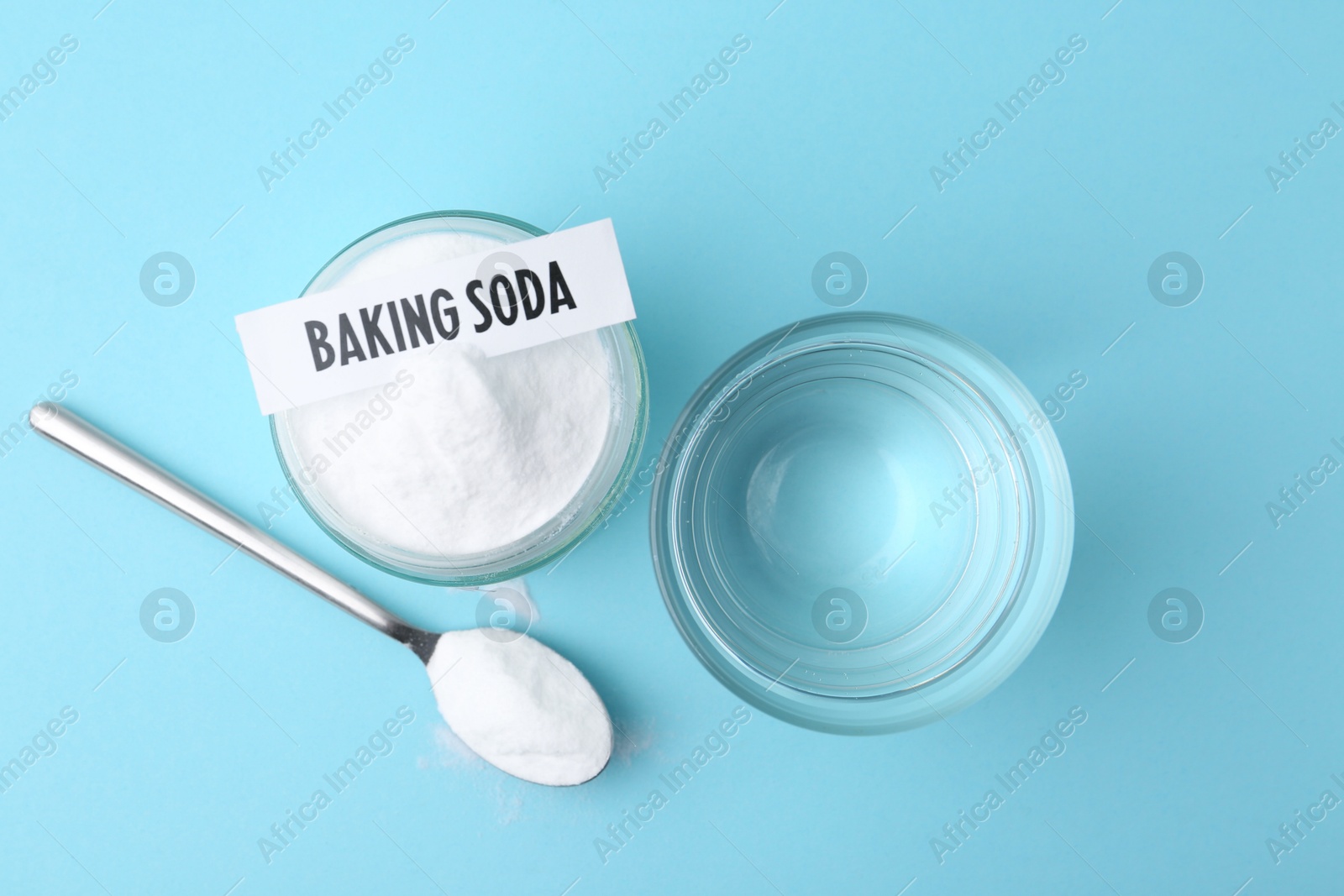 Photo of Glass of water and baking soda on light blue background, top view