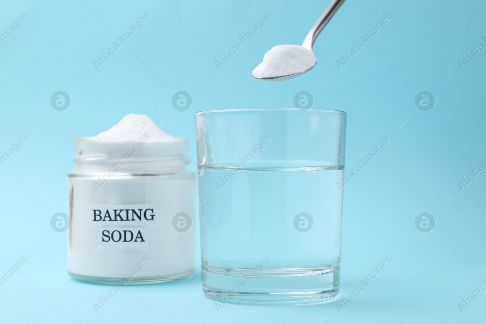 Photo of Glass of water and baking soda on light blue background