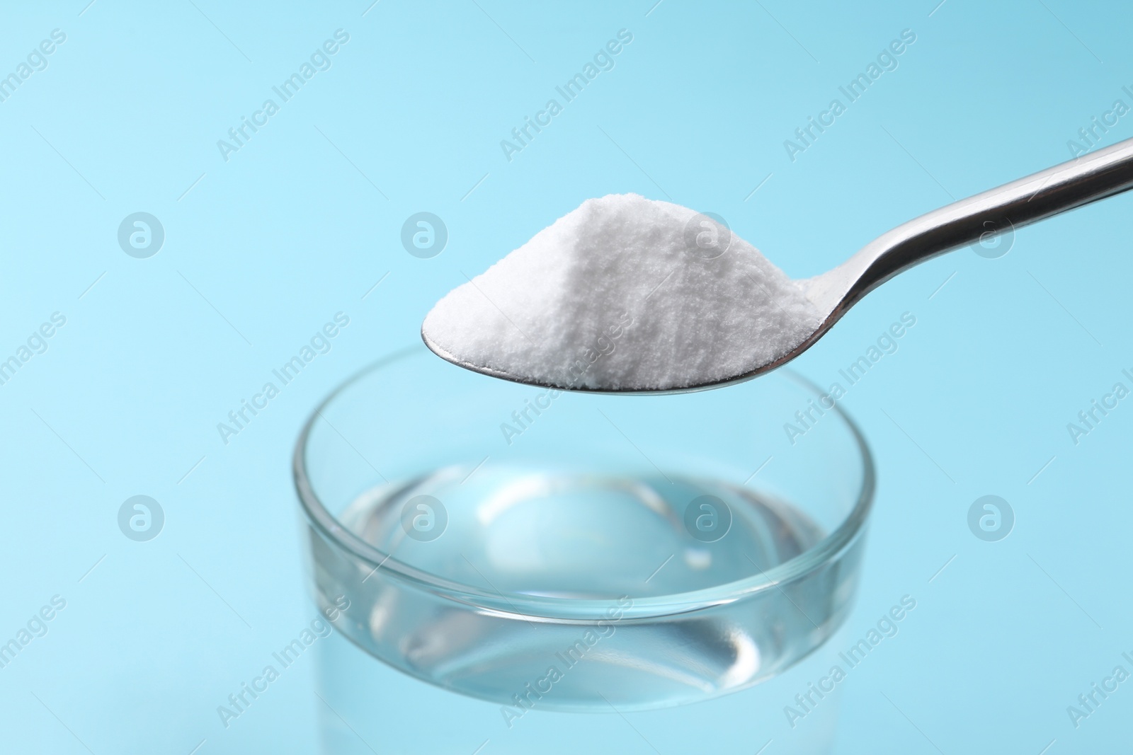 Photo of Adding baking soda to glass of water on light blue background, closeup