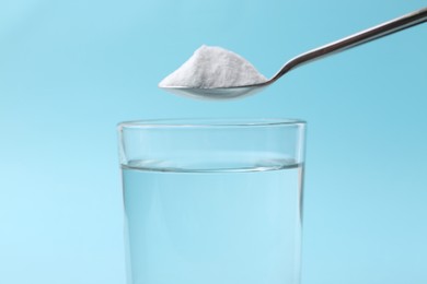 Photo of Adding baking soda to glass of water on light blue background, closeup