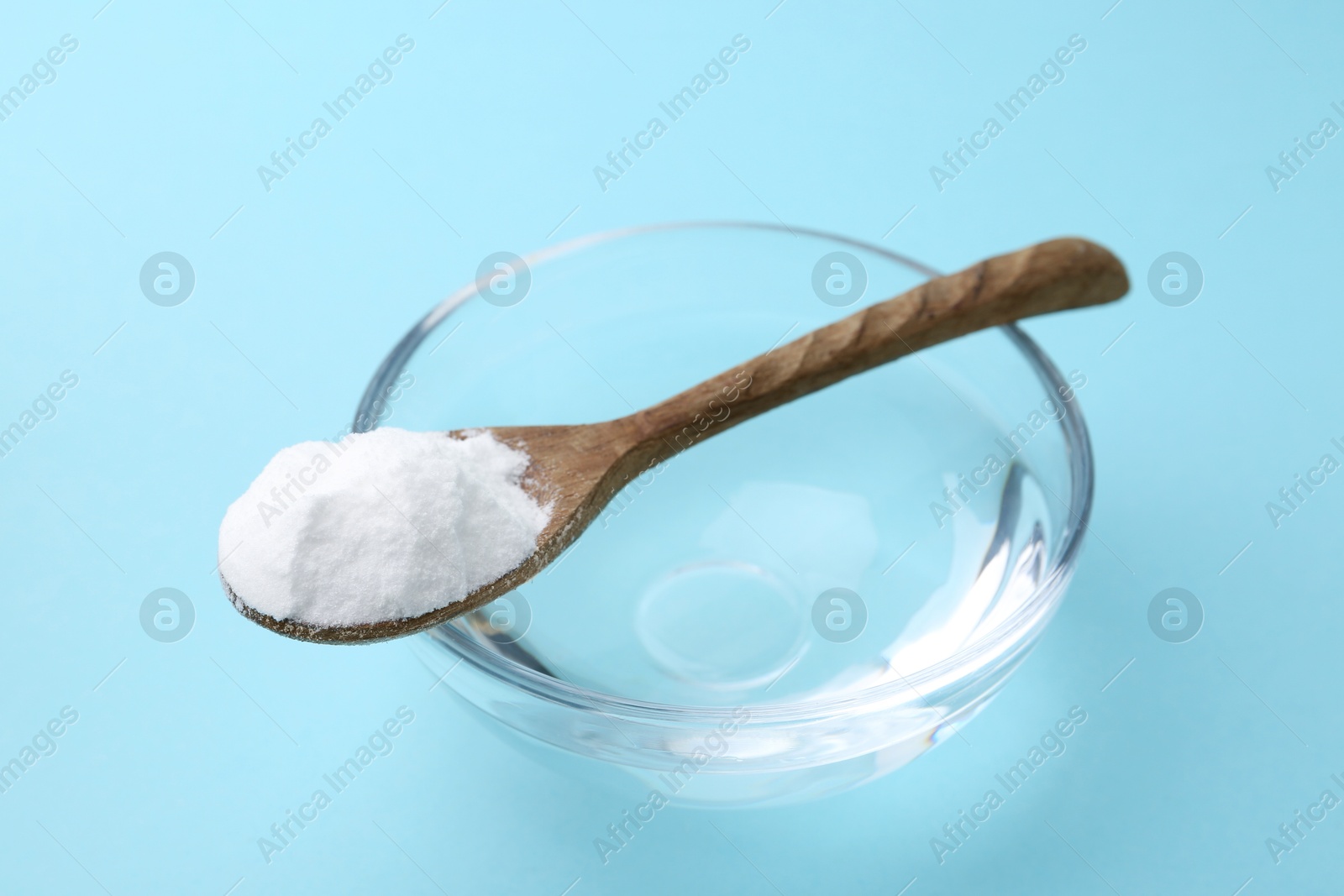 Photo of Glass of water and baking soda on light blue background, closeup