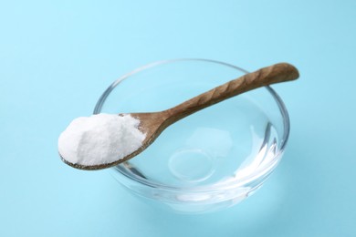 Photo of Glass of water and baking soda on light blue background, closeup