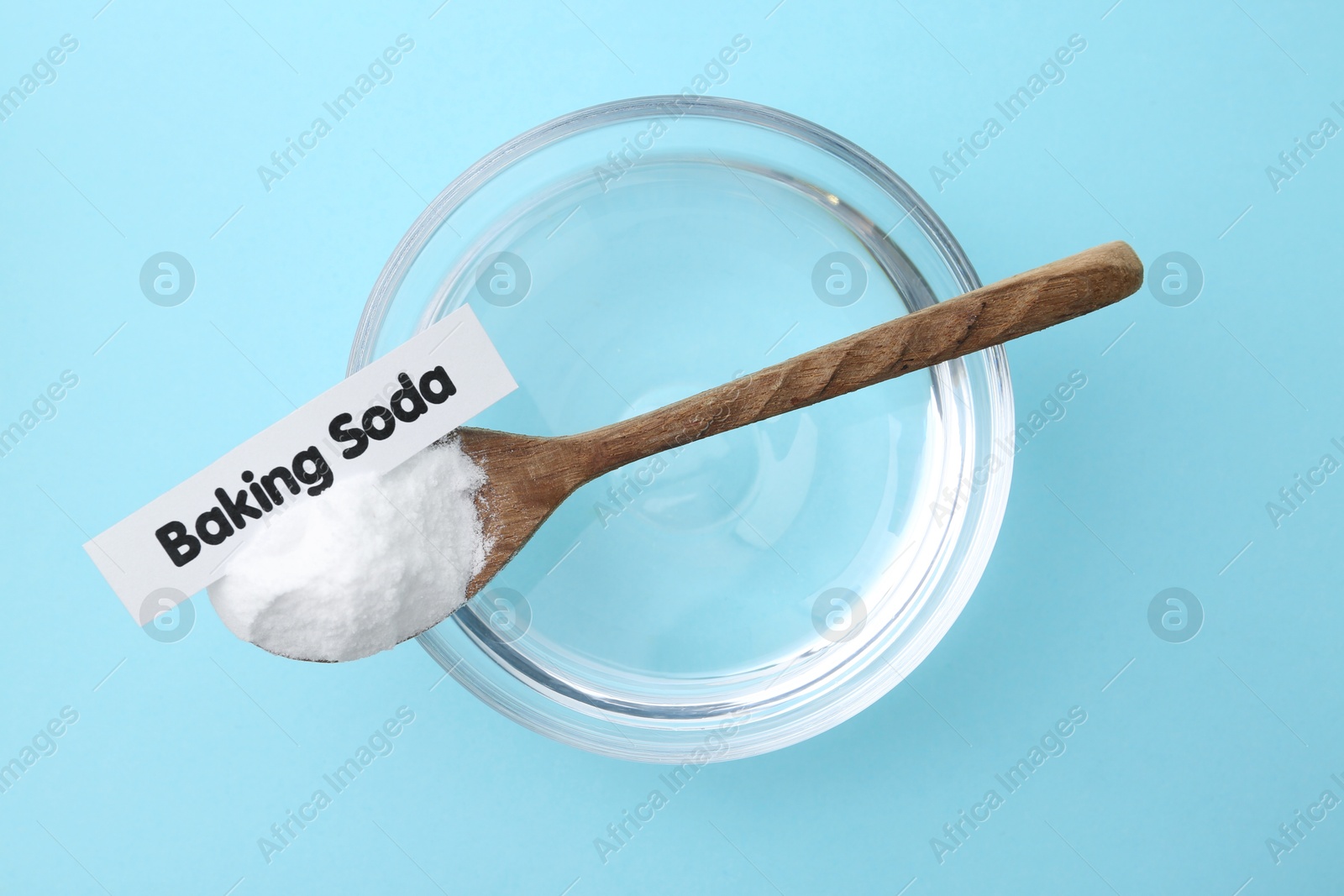 Photo of Glass of water and baking soda on light blue background, top view