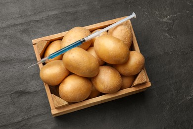 Photo of GMO concept. Potatoes and syringe with liquid in crate on dark textured table, top view