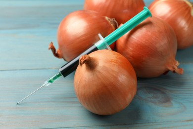 Photo of GMO concept. Onion bulbs and syringe with liquid on light blue wooden table, closeup