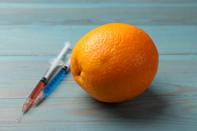 Photo of GMO concept. Orange and syringes with liquid on light blue wooden table, closeup