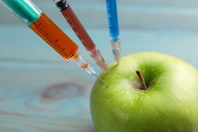 Photo of GMO concept. Green apple with syringes on blurred background, closeup