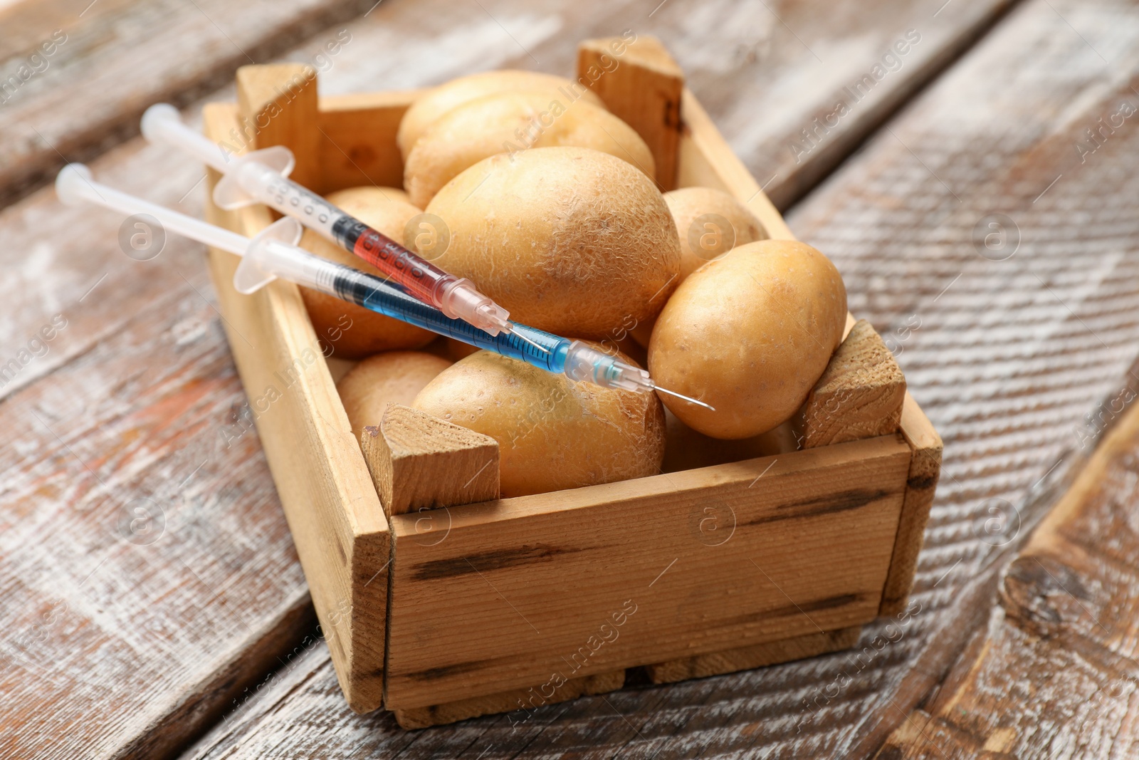 Photo of GMO concept. Potatoes in crate and syringes with liquid on rustic wooden table, closeup