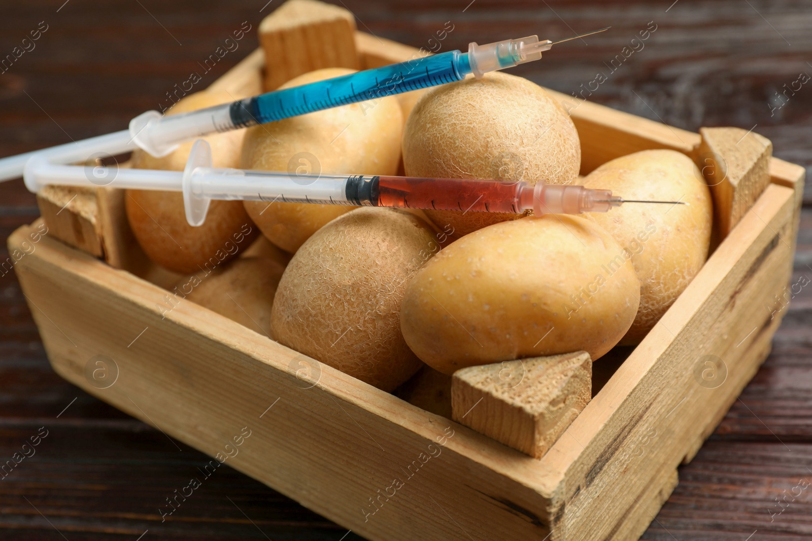 Photo of GMO concept. Potatoes in crate and syringes with liquid on wooden table, closeup