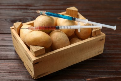 Photo of GMO concept. Potatoes in crate and syringes with liquid on wooden table, closeup