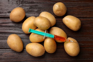 Photo of GMO concept. Potatoes and syringe on wooden table, flat lay