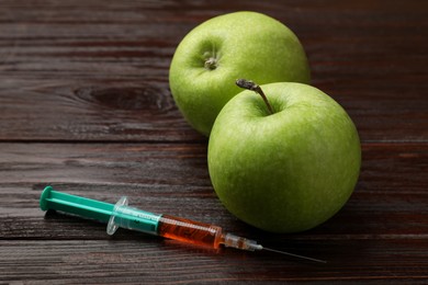 Photo of GMO concept. Green apples and syringe on wooden table, closeup