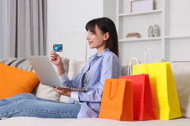 Photo of Internet shopping. Happy woman with credit card, laptop and colorful bags on sofa at home