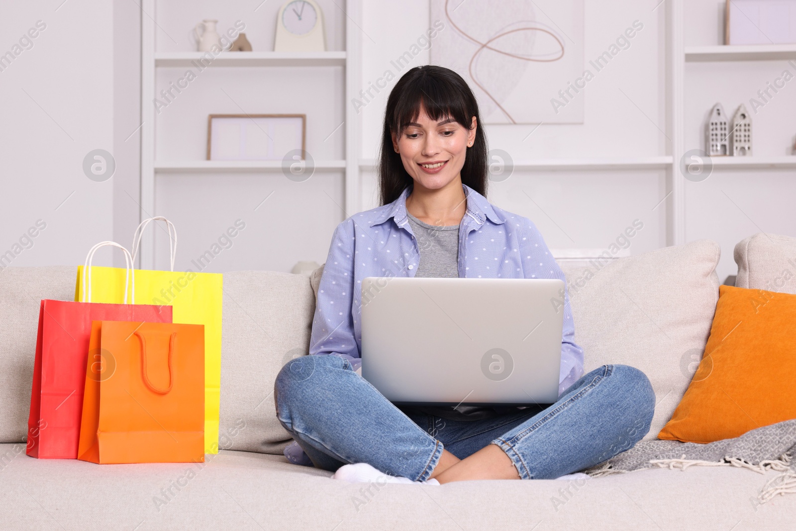 Photo of Internet shopping. Happy woman with laptop and colorful bags on sofa at home