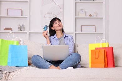 Photo of Internet shopping. Happy woman with credit card, laptop and colorful bags on sofa at home