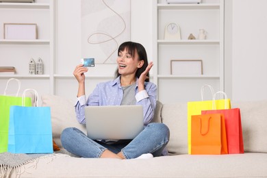 Photo of Internet shopping. Happy woman with credit card, laptop and colorful bags on sofa at home