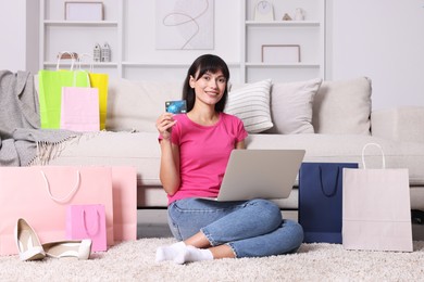 Internet shopping. Happy woman with credit card, laptop and colorful bags at home