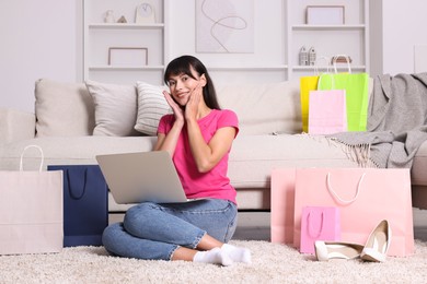 Photo of Internet shopping. Happy woman with laptop and colorful bags at home