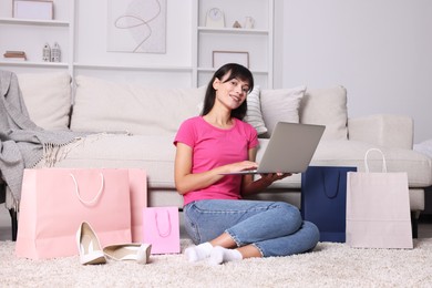 Photo of Internet shopping. Happy woman with laptop and colorful bags at home