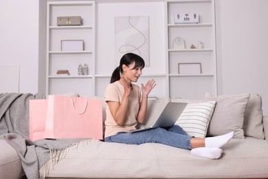 Photo of Internet shopping. Happy woman with laptop and colorful bags on sofa at home