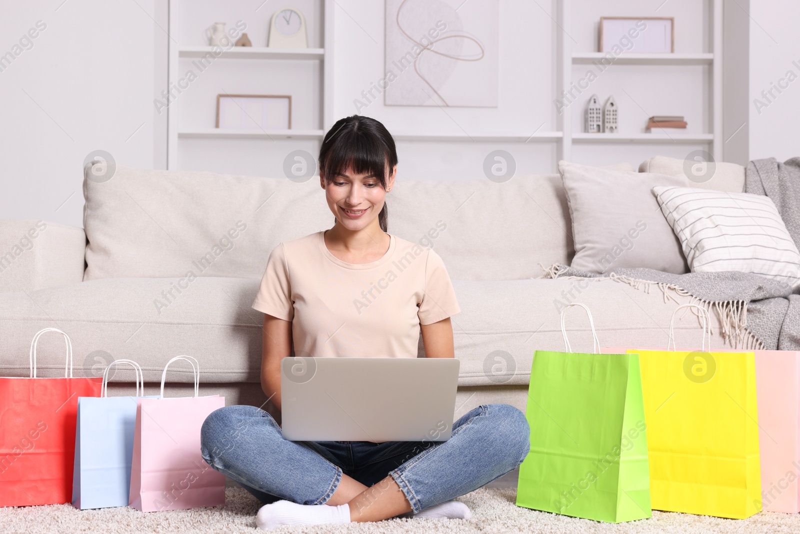 Photo of Internet shopping. Happy woman with laptop and colorful bags at home