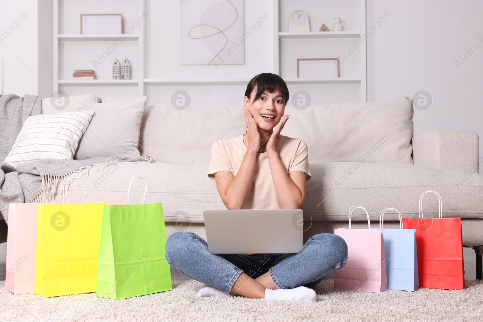 Photo of Internet shopping. Happy woman with laptop and colorful bags at home