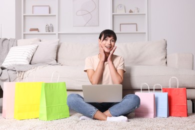 Photo of Internet shopping. Happy woman with laptop and colorful bags at home