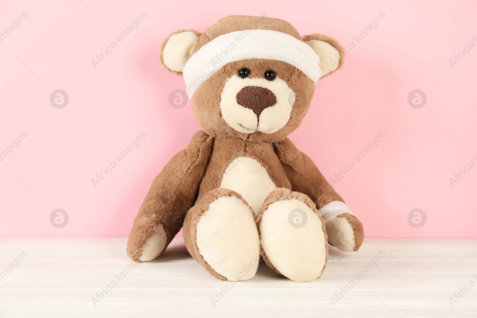 Photo of Teddy bear with bandages on white wooden table against pink background