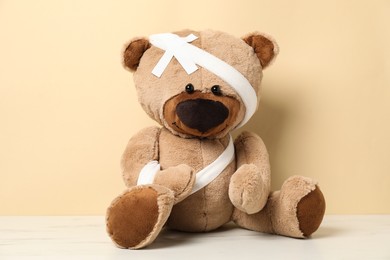 Photo of Teddy bear with bandages and sticking plasters on white marble table against beige background