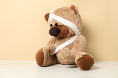Photo of Teddy bear with bandages and sticking plasters on white marble table against beige background
