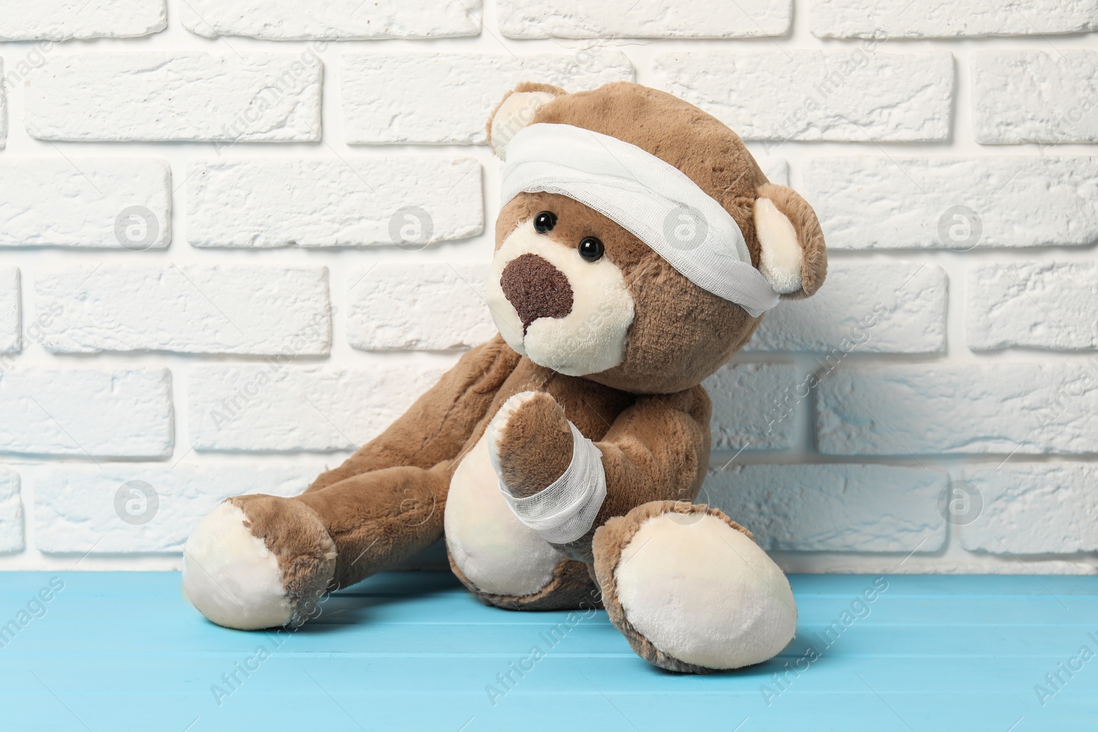 Photo of Teddy bear with bandages on light blue wooden table against white brick wall