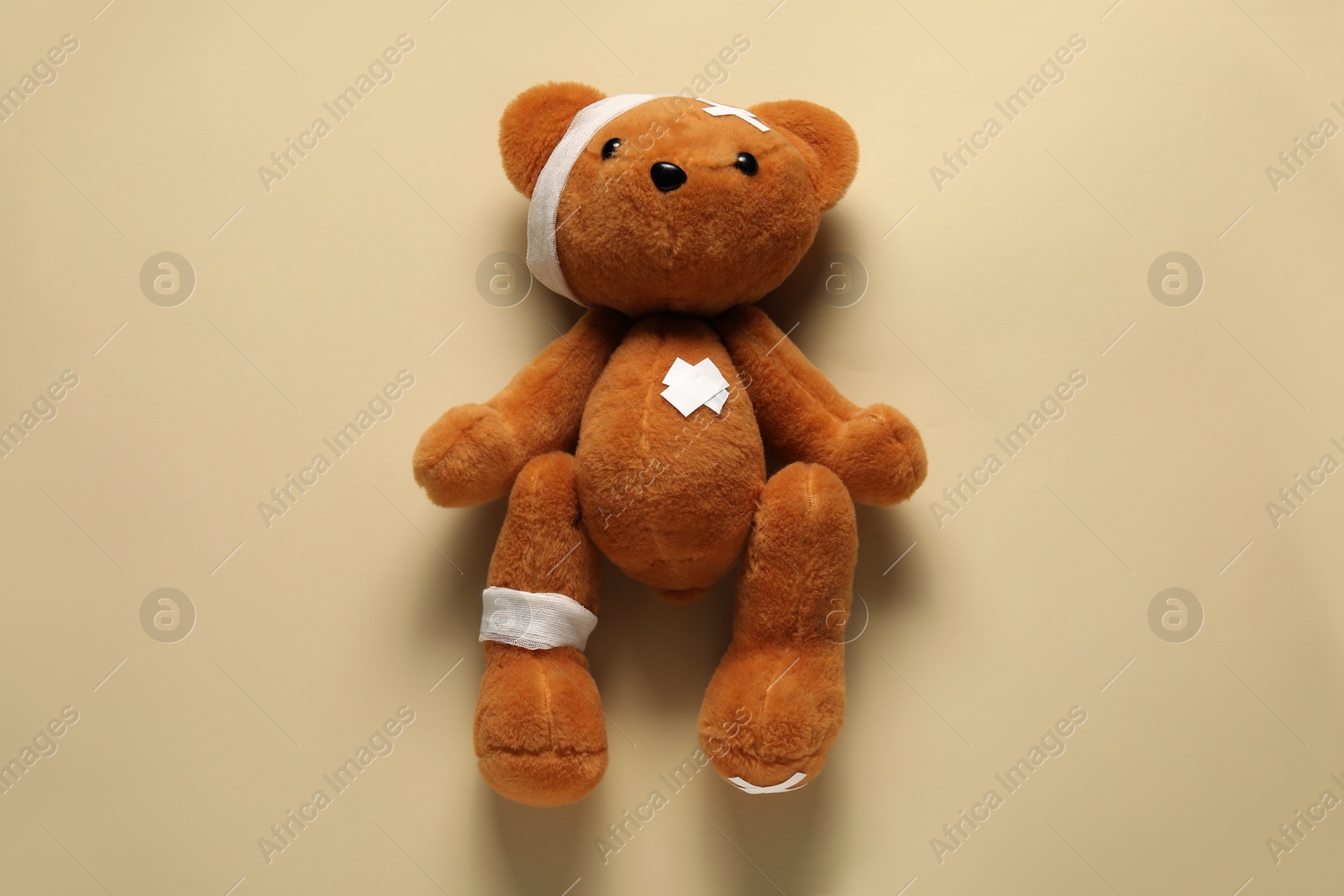 Teddy bear with bandages and sticking plasters on beige background, top view Photo of Teddy bear with bandages and sticking plasters on beige background, top view