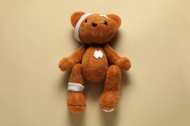 Photo of Teddy bear with bandages and sticking plasters on beige background, top view