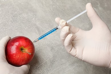 Photo of GMO concept. Scientist injecting something into fresh apple at grey table, closeup