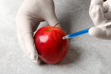 Photo of GMO concept. Scientist injecting something into fresh apple at grey table, closeup