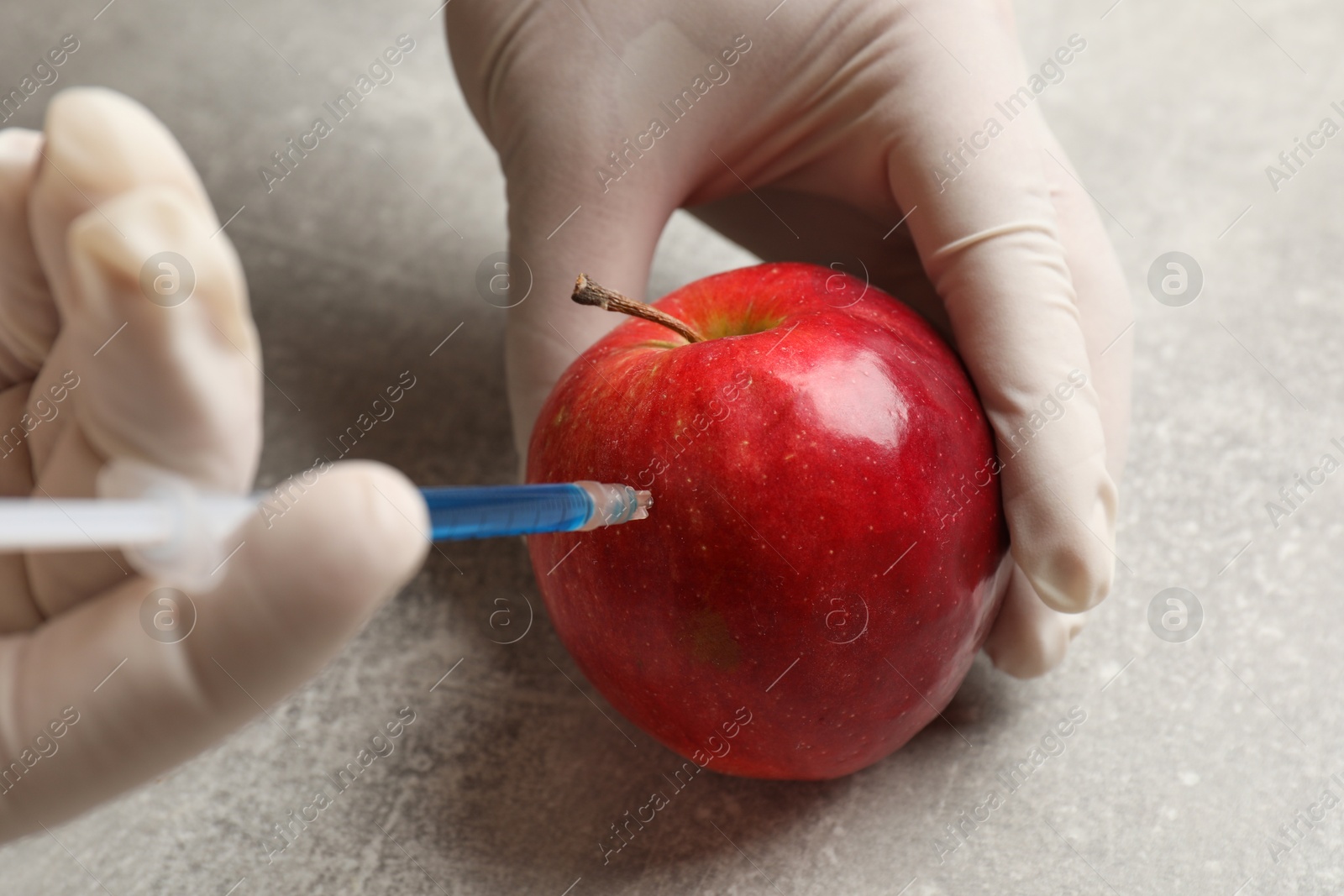 Photo of GMO concept. Scientist injecting something into fresh apple at grey table, closeup