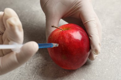 Photo of GMO concept. Scientist injecting something into fresh apple at grey table, closeup